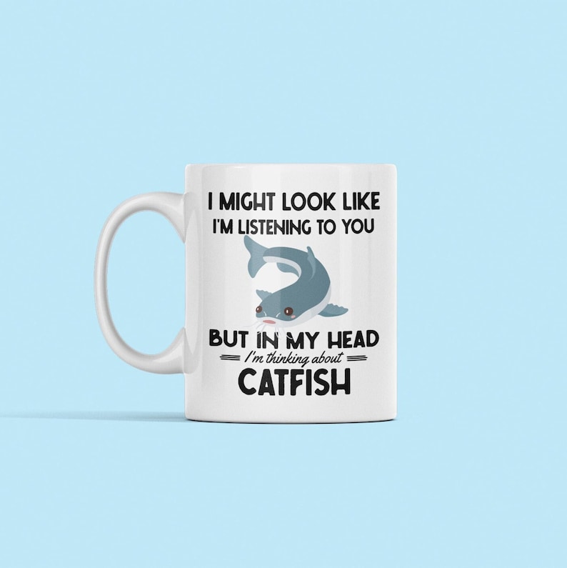 May include: White ceramic mug with a black and white graphic of a catfish. The text on the mug reads "I might look like I'm listening to you but in my head I'm thinking about catfish."