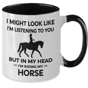 May include: White ceramic mug with a black rim and handle. The mug has a black silhouette of a person riding a horse with the text "I might look like I'm listening to you but in my head I'm riding my horse."