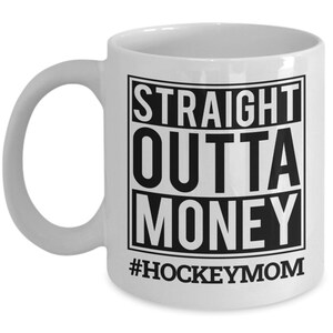 May include: White ceramic coffee mug with a black graphic that reads "STRAIGHT OUTTA MONEY #HOCKEYMOM".