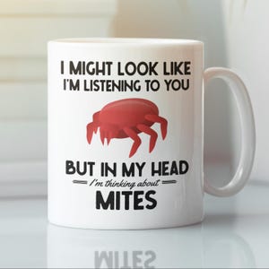 Puede incluir: Taza de cerámica blanca con una ilustración de ácaro rojo y el texto "Puede que parezca que te estoy escuchando, pero en mi cabeza estoy pensando en ácaros."
