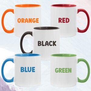 May include: Five ceramic mugs with colored rims. The mugs are white with the words "ORANGE", "RED", "BLACK", "BLUE", and "GREEN" printed in bold, black letters.