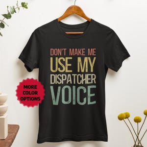 Op de afbeelding: Zwart T-shirt met een vintage-stijl grafische afbeelding met de tekst "Maak me niet mijn dispatcher stem gebruiken".