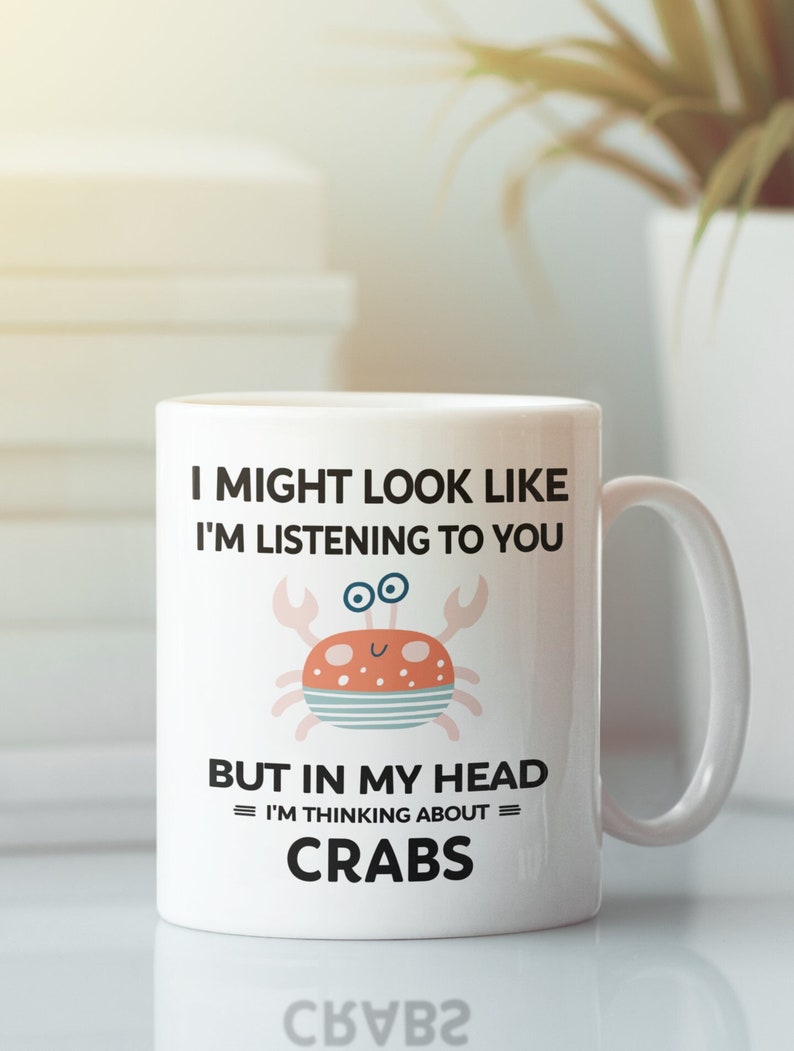 Pu&ograve; includere: Una tazza in ceramica bianca con un grafico in bianco e nero di un granchio. Il testo sulla tazza recita "I might look like I'm listening to you but in my head I'm thinking about = CRABS =."