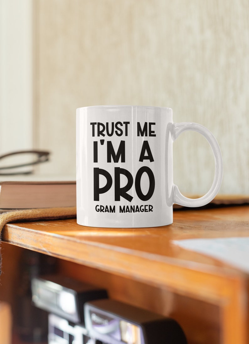 May include: White ceramic mug with black text that reads "Trust me I'm a pro Gram Manager".