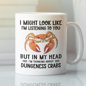 May include: White ceramic mug with a black and orange crab illustration. The mug reads "I might look like I'm listening to you, but in my head I'm thinking about Dungeness Crabs."