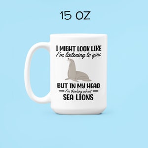 May include: White ceramic mug with a black and grey sea lion illustration. The mug reads "I might look like I'm listening to you, but in my head I'm thinking about sea lions".