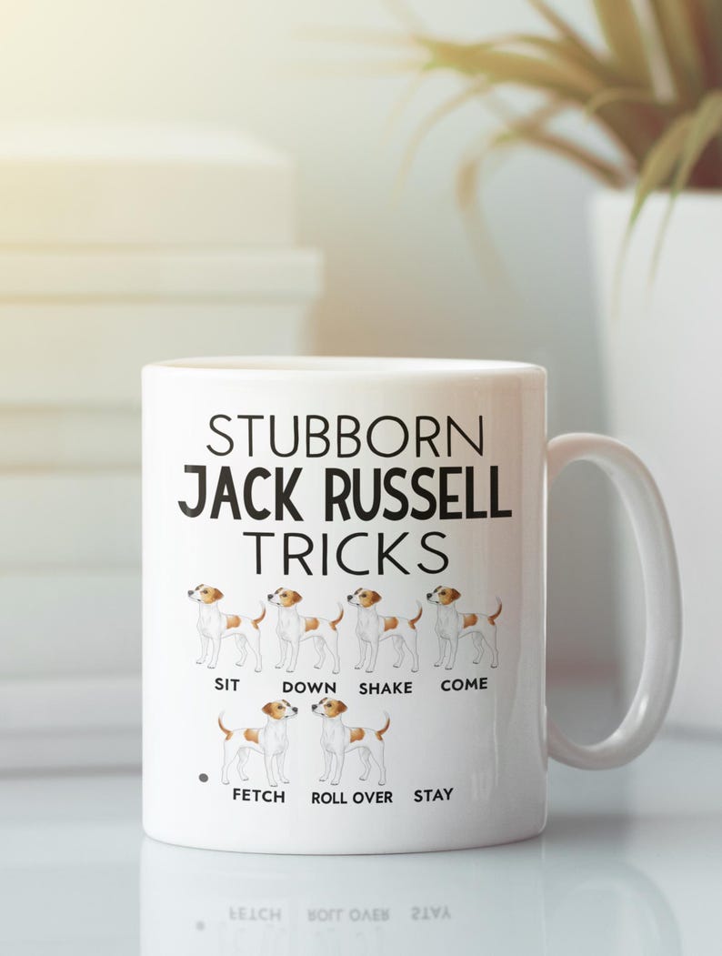 May include: White ceramic mug featuring the text "STUBBORN JACK RUSSELL TRICKS" with illustrations of a Jack Russell Terrier demonstrating tricks. The tricks include "SIT", "DOWN", "SHAKE", "COME", "FETCH", "ROLL OVER", and "STAY".