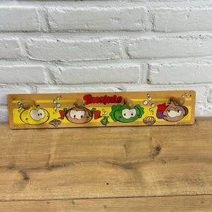 May include: A vintage wooden coat rack with cartoon characters and the word "Snorkels" in red. The rack has four wooden pegs. The characters are painted in yellow, green, orange, and purple.