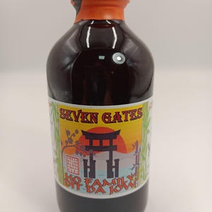 May include: A dark brown liquid in a clear glass bottle with an orange cap. The label features the text SEVEN GATES and HO FAMILY DIT DA JOW, with a graphic of a black torii gate, a red sun, and green bamboo stalks against a light blue background.