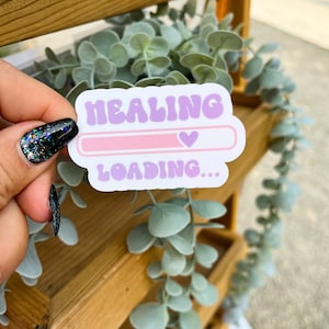 May include: A sticker with a purple and pink design that reads "HEALING LOADING..." with a pink progress bar and a pink heart icon.