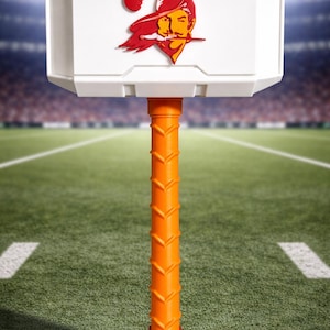 May include: A white and orange novelty hammer featuring the Tampa Bay Buccaneers logo. The hammer has a white head with the team logo and an orange handle with a red base. The background is a football field.