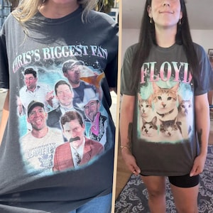May include: A charcoal gray t-shirt featuring a collage of a man in various poses and outfits with the text CHRIS'S BIGGEST FAN, alongside a second charcoal gray t-shirt displaying a group of five cats and the word FLOYD in pink and white.