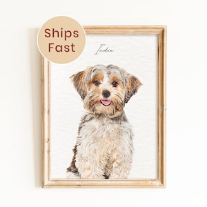May include: A framed portrait of a small dog with tan, brown, and white fur, featuring the name Indie written in black script above the dog's head. The artwork is displayed in a light-colored wooden frame against a plain white background.