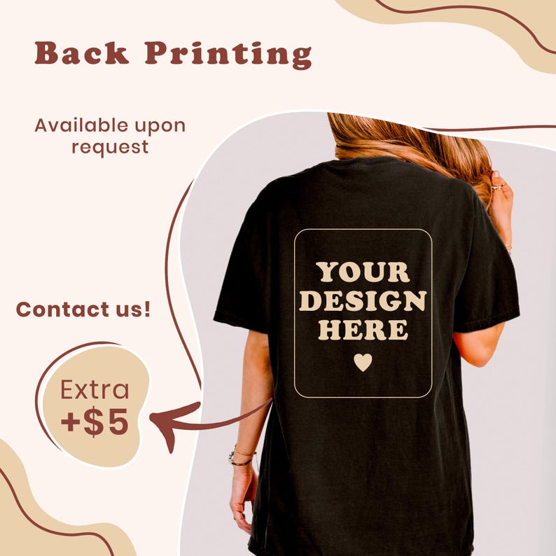 May include: A black t-shirt featuring a rectangular graphic on the back with the text "YOUR DESIGN HERE" in a beige, wavy font, accompanied by a small heart icon. The design is centered on the back of the shirt, which is shown from behind.