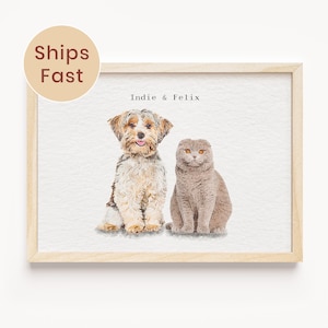 May include: A framed watercolor print featuring a dog and a cat. The dog has brown and white fur, and the cat is gray. The print is labeled "Indie & Felix" and has a "Ships Fast" sticker.