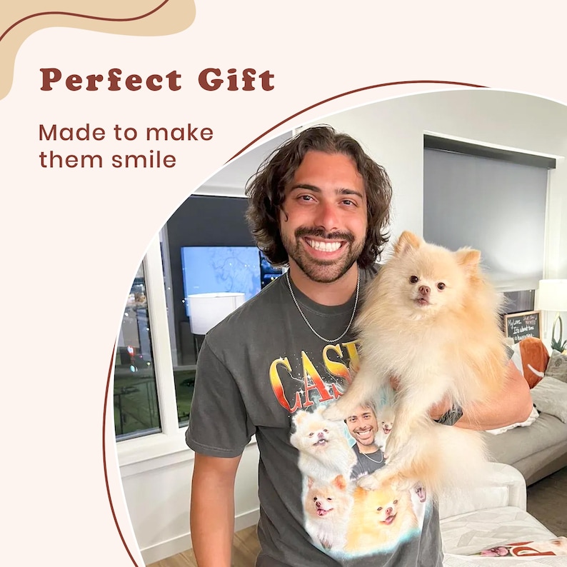 May include: A charcoal gray short-sleeve t-shirt featuring a graphic print of multiple Pomeranian dogs and a person's face. The shirt has a crew neckline and is worn by a person holding a light-colored, fluffy Pomeranian dog in their arms.