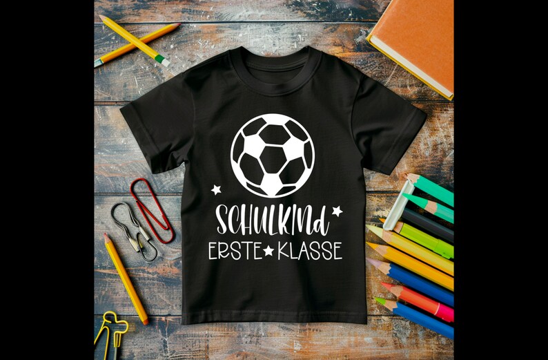 May include: Black t-shirt with a white soccer ball graphic and the text "SCHULKIND ERSTE KLASSE" in white.