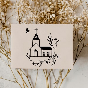 May include: A black and white illustration of a church with a heart on the steeple, surrounded by floral sprigs. The illustration is on a white card.
