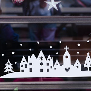 May include: White silhouette of a small town with a church, houses, and trees on a snowy background. The design is perfect for a Christmas window cling.