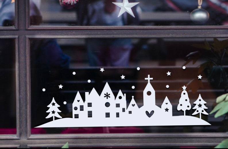 May include: White silhouette of a small town with a church, houses, and trees on a snowy background. The design is perfect for a Christmas window cling.