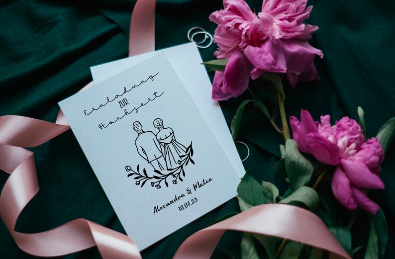 May include: A white wedding invitation with black calligraphy that reads "Einladung zur Hochzeit" and a simple line drawing of a couple holding hands. The text below the drawing reads "Alexandra & Mateo 10.07.23". The invitation is surrounded by pink peonies and a pink ribbon.