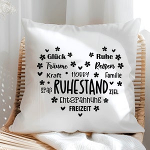 May include: White square pillow with a black heart-shaped design. The design includes the word "RUHESTAND" and other German words like "Gl&uuml;ck", "Tr&auml;ume", "Ruhe", "Reisen", "Familie", "Freizeit", and "Entspannung".