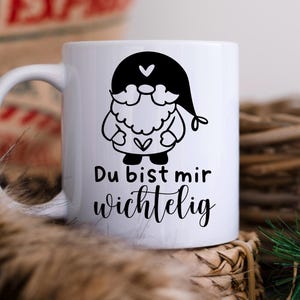 K&ouml;nnte beinhalten: Wei&szlig;e Keramiktasse mit einer schwarz-wei&szlig;en Illustration eines Gnoms mit einem Herzen auf der Brust. Der Text "Du bist mir wichtig" ist auf die Tasse gedruckt.