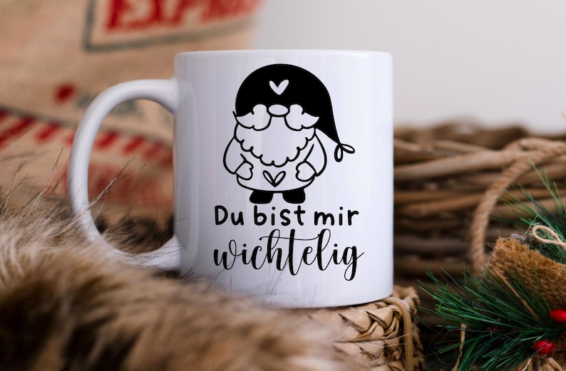 K&ouml;nnte beinhalten: Wei&szlig;e Keramiktasse mit einer schwarz-wei&szlig;en Illustration eines Gnoms mit einem Herzen auf der Brust. Der Text "Du bist mir wichtig" ist auf die Tasse gedruckt.