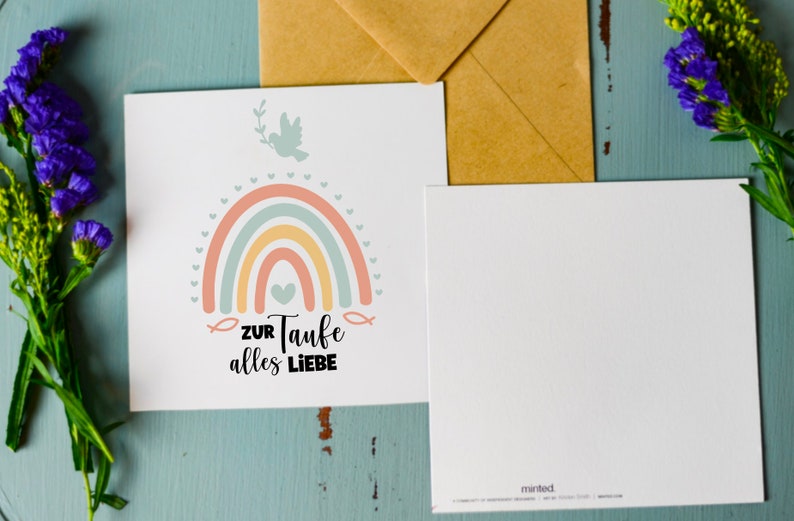 May include: A white card with a rainbow, a dove, and the text "ZUR Taufe alles LIEBE" in black. The card is on a blue wooden surface with a brown envelope and purple flowers.