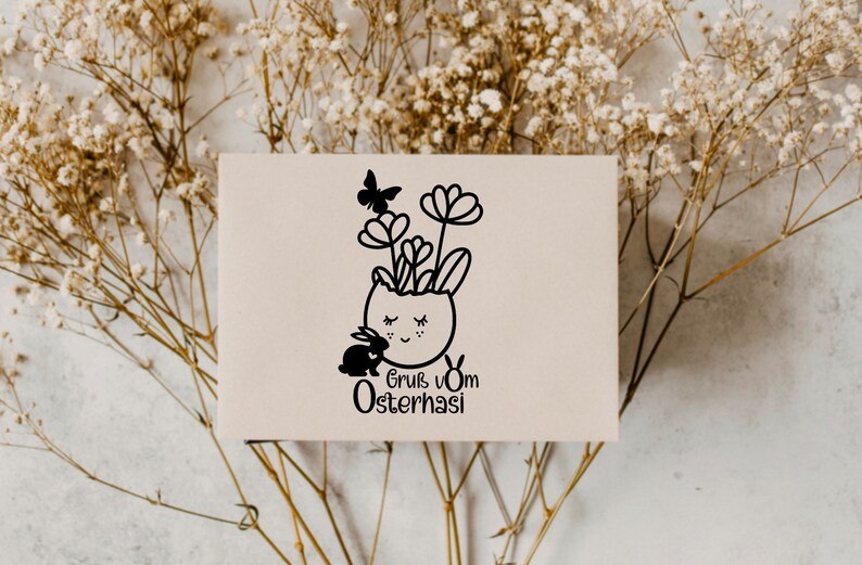 May include: A white card with a black and white illustration of a bunny in an egg-shaped pot with flowers and a butterfly. The text "Gruss vom Osterhasi" is below the illustration.