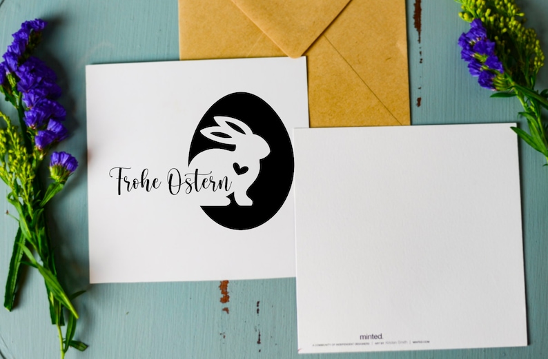 May include: A white card with a black circle containing a white silhouette of a rabbit with a heart. The text "Frohe Ostern" is written in black cursive script below the circle.