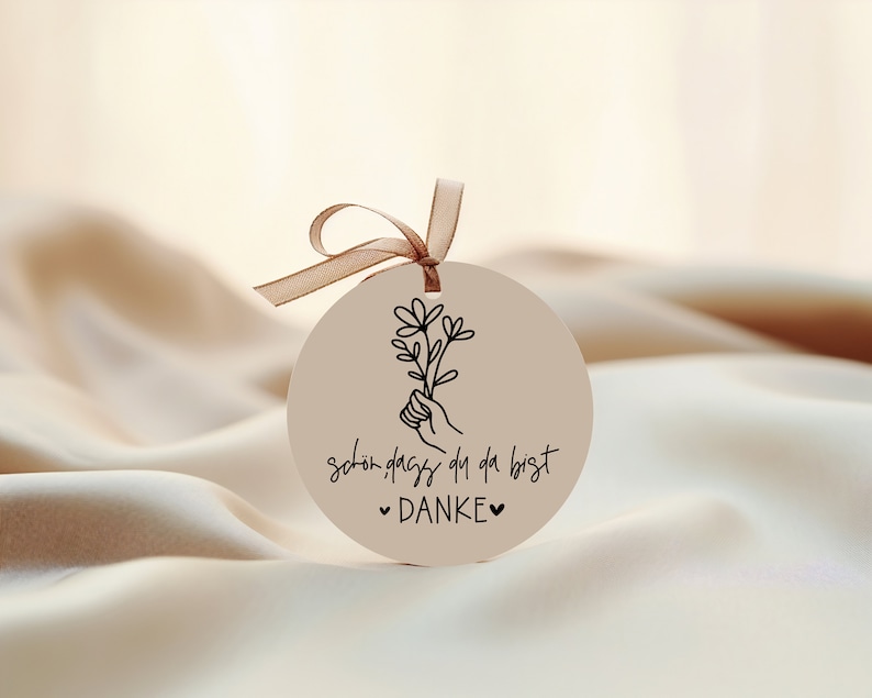 Peut inclure: Une &eacute;tiquette ronde de couleur cr&egrave;me avec une illustration en noir et blanc d'une main tenant un bouquet de fleurs. L'&eacute;tiquette porte le texte "sch&ouml;n dass du da bist &hearts; DANKE &hearts;" imprim&eacute; dessus.