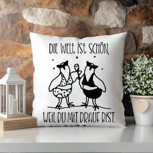May include: White square cushion featuring a black illustration of two birds, one holding a glass. The cushion has the German text "DIE WELT IST SCH&Ouml;N, WEIL DU MIT DRAUF BIST." Decorative cushion for home decor.