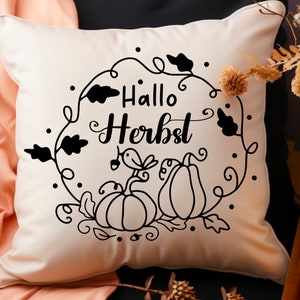 May include: A white throw pillow with black text that says "Hallo Herbst" in a decorative font. The text is surrounded by a wreath of leaves and pumpkins.