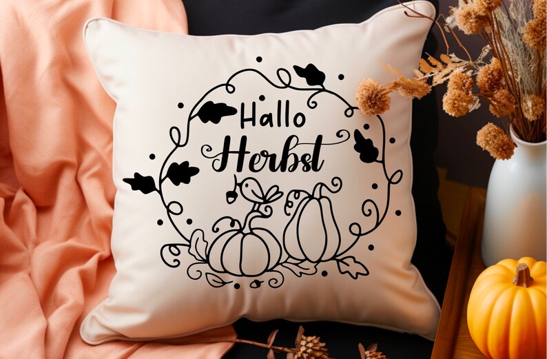 May include: A white throw pillow with black text that says "Hallo Herbst" in a decorative font. The text is surrounded by a wreath of leaves and pumpkins.
