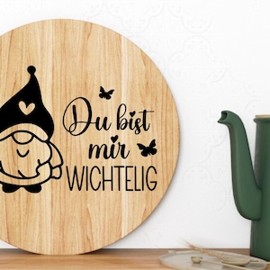 K&ouml;nnte beinhalten: Ein rundes, h&ouml;lzernes Schneidebrett mit einem schwarz-wei&szlig;en Gnom-Design und dem Text "Du bist mir wichtig", was "Du bist mir wichtig" bedeutet.