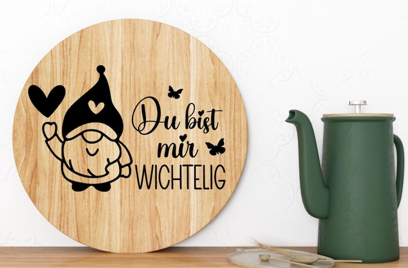 K&ouml;nnte beinhalten: Ein rundes, h&ouml;lzernes Schneidebrett mit einem schwarz-wei&szlig;en Gnom-Design und dem Text "Du bist mir wichtig", was "Du bist mir wichtig" bedeutet.