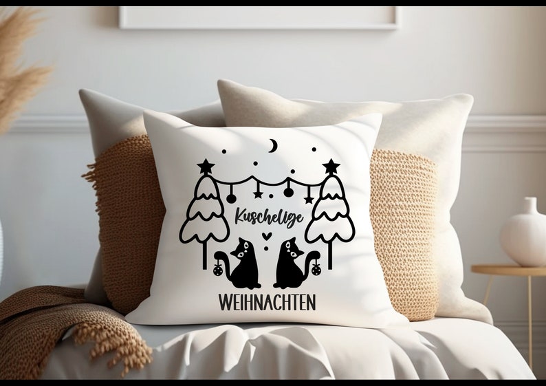 May include: White throw pillow with black text and illustrations. The text reads "Kuschelige Weihnachten" which translates to "Cozy Christmas" in English. The illustration features two black cats sitting under a string of lights between two Christmas trees.