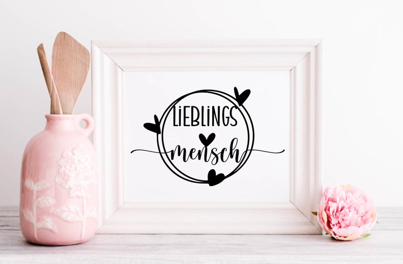 May include: A white framed print with black text that reads "Lieblingsmensch" in a circle with hearts around it.