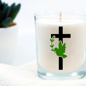 May include: A white candle in a glass jar with a black cross and a green dove with an olive branch behind it.