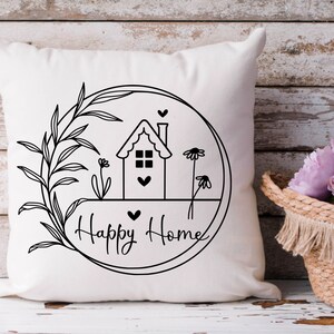 May include: White cushion with a black and white illustration of a house with a heart, flowers, and leaves inside a circle. The text "Happy Home" is written below the circle.