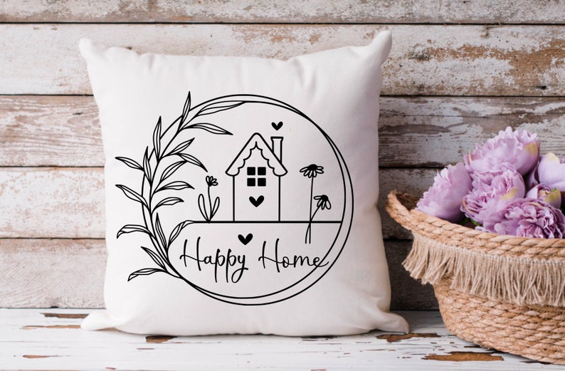 May include: White cushion with a black and white illustration of a house with a heart, flowers, and leaves inside a circle. The text "Happy Home" is written below the circle.