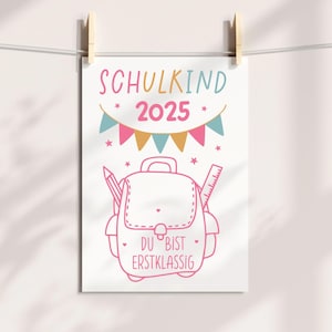 May include: A white poster with a pink outline illustration of a backpack, pencil, and ruler. The text "SCHULKIND 2025" is at the top, with the words "DU BIST ERSTKLASSIG" at the bottom. The poster is held by wooden clothespins.