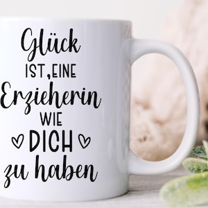 May include: White ceramic mug with a black inscription in German: "Gl&uuml;ck ist, eine Erzieherin wie DICH zu haben" (Happiness is having a teacher like YOU). The mug has a curved handle and is set against a blurred background.