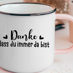 Puede incluir: Taza de esmalte blanco con borde negro y asa rosa. La taza tiene texto negro que dice "Danke dass du immer da bist" con un peque&ntilde;o coraz&oacute;n a cada lado de la palabra "Danke".