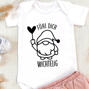 K&ouml;nnte beinhalten: Wei&szlig;er Baby-Strampler mit einer schwarz-wei&szlig;en Illustration eines Zwergs, der einen Herzballon h&auml;lt. Der Text "F&uuml;hl dich wichtig" ist unter dem Zwerg gedruckt.