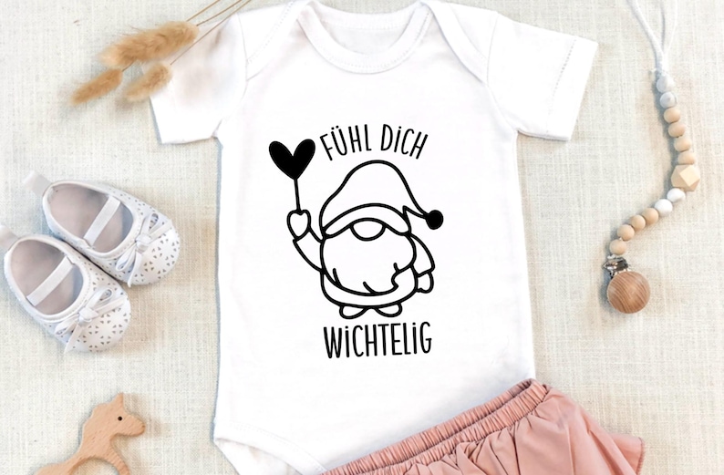 K&ouml;nnte beinhalten: Wei&szlig;er Baby-Strampler mit einer schwarz-wei&szlig;en Illustration eines Zwergs, der einen Herzballon h&auml;lt. Der Text "F&uuml;hl dich wichtig" ist unter dem Zwerg gedruckt.