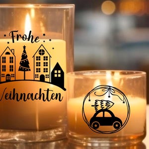 May include: Two glass candle jars with a warm glow. The larger jar has a black and white design of houses and a Christmas tree with the text "Frohe Weihnachten". The smaller jar has a black and white design of a car with a Christmas tree on top, surrounded by a circle.