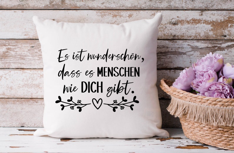 May include: White throw pillow with black text that reads "Es ist wundersch&ouml;n, dass es Menschen wie DICH gibt."  The text is surrounded by two small floral designs with a heart in the center.