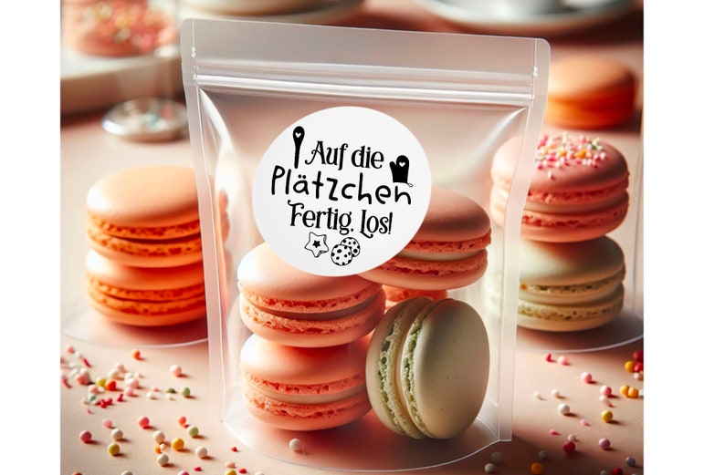 May include: A clear plastic bag filled with pastel pink and green macarons. The bag has a white sticker with black text that reads "Auf die Pl&auml;tzchen Fertig. Los!"